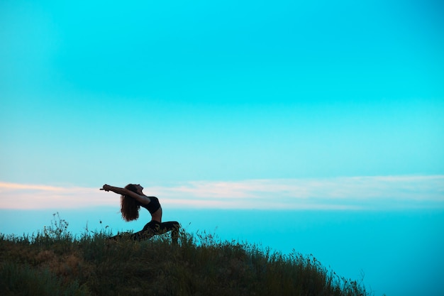 Die Silhouette der jungen Frau praktiziert Yoga