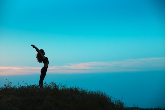 Die Silhouette der jungen Frau praktiziert Yoga