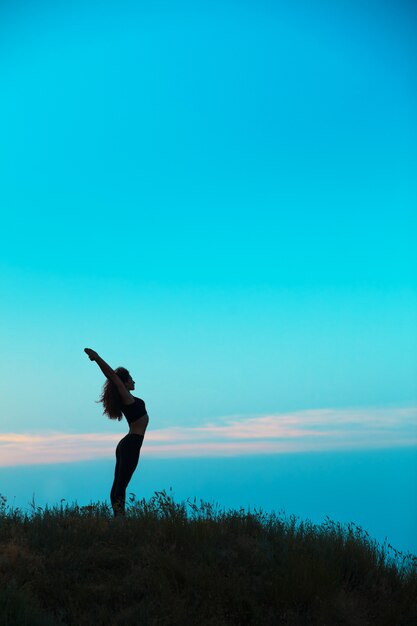 Die Silhouette der jungen Frau praktiziert Yoga