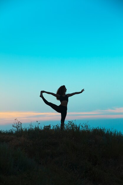 Die Silhouette der jungen Frau praktiziert Yoga