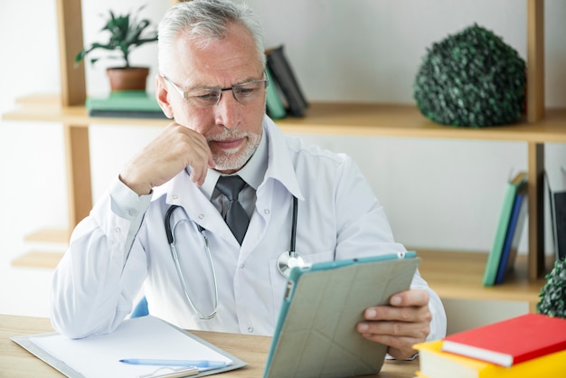 Die Stirn runzelnder Doktor, der Tablette im Büro verwendet