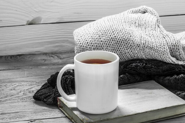 die Tasse Tee auf einem schönen hölzernen Hintergrund mit Winterpullover, altem Buch, Winter, Herbst, Nahaufnahme