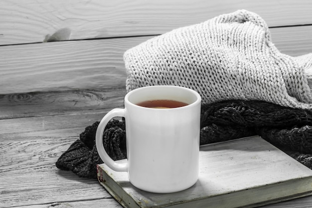 die Tasse Tee auf einem schönen hölzernen Hintergrund mit Winterpullover, altem Buch, Winter, Herbst, Nahaufnahme