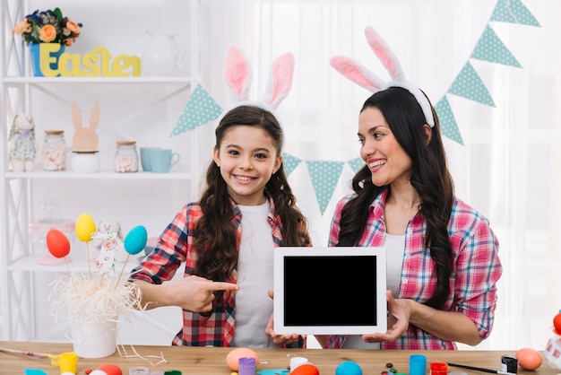 Die tochter, die finger auf den digitalen tablettengriff zeigt, halten durch ihre mutter an ostern-tag