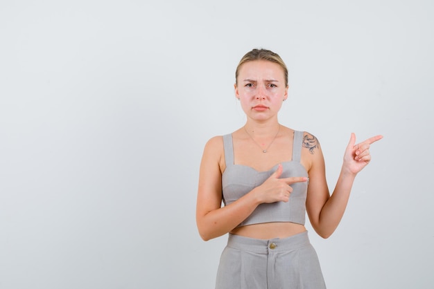 Die traurige junge frau zeigt mit ihrem zeigefinger auf weißem hintergrund nach rechts