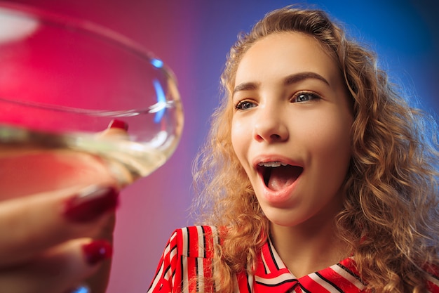 Die überraschte junge Frau in Partykleidung posiert mit einem Glas Wein