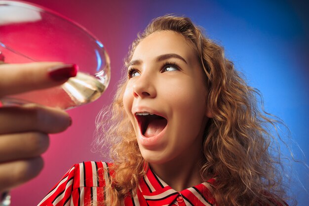 Die überraschte junge Frau in Partykleidung posiert mit einem Glas Wein.