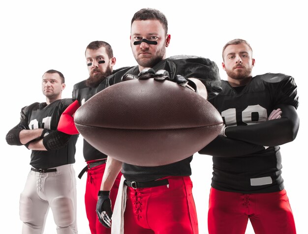 Die vier kaukasischen Fitness-Männer als American-Football-Spieler posieren in voller Länge mit einem Ball auf Weiß