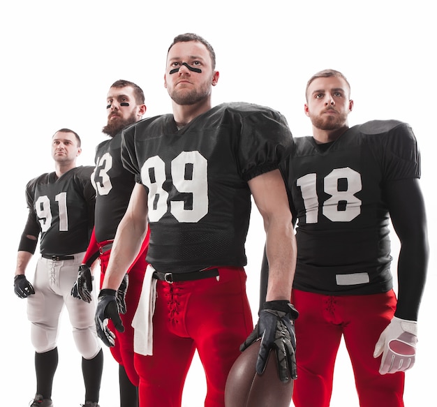 Die vier kaukasischen Fitnessmänner als American-Football-Spieler posieren in voller Länge mit einem Ball auf weißem Hintergrund