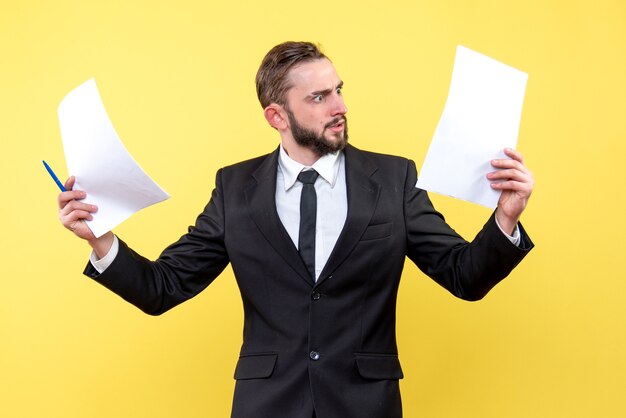 Die Vorderansicht des verwirrten Geschäftsmanns des jungen Mannes in einem Anzug schaut empört auf das leere Papier auf Gelb