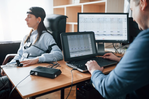 Die Wahrheit überprüfen. Mädchen geht Lügendetektor im Büro vorbei. Fragen stellen. Polygraphentest