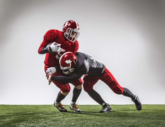 Die zwei American-Football-Spieler in Aktion auf grünem Gras und grauem Hintergrund.