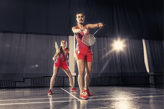 Die zwei jungen Frauen spielen Badminton über Fitnessraum. Konzeptspiel zu zweit