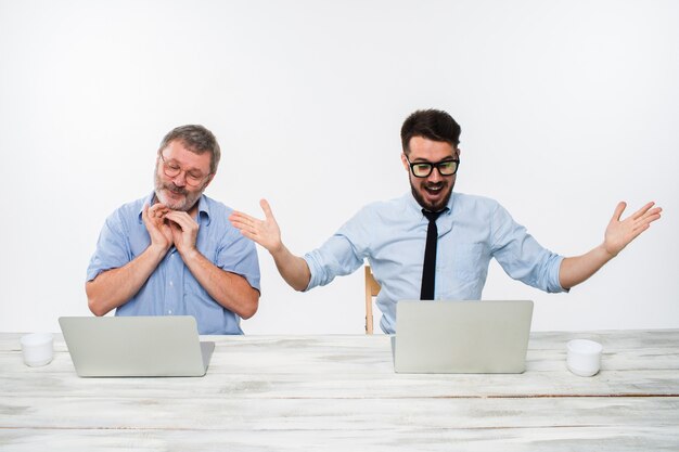 Die zwei Kollegen arbeiten zusammen im Büro auf weißem Hintergrund. beide schauen auf die Computerbildschirme. Beide überrascht. Konzept der positiven Emotionen und guten Nachrichten