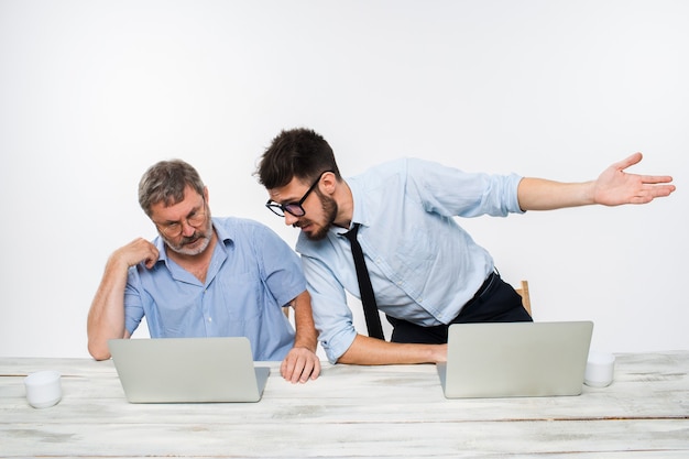 Die zwei Kollegen arbeiten zusammen im Büro auf weißem Hintergrund. Sie diskutieren etwas. beide schauen auf einen Computerbildschirm
