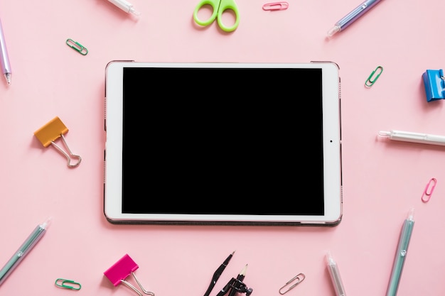 Digital-Tablette umgeben durch verschiedene Schreibwarengeschäfte auf rosa Hintergrund