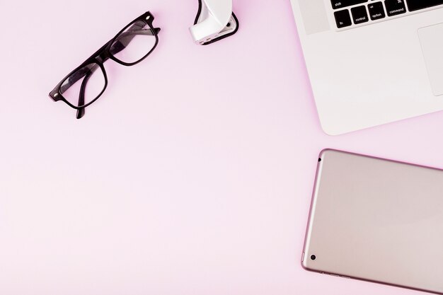 Digitale Tablette; Brille und Laptop auf rosa Hintergrund