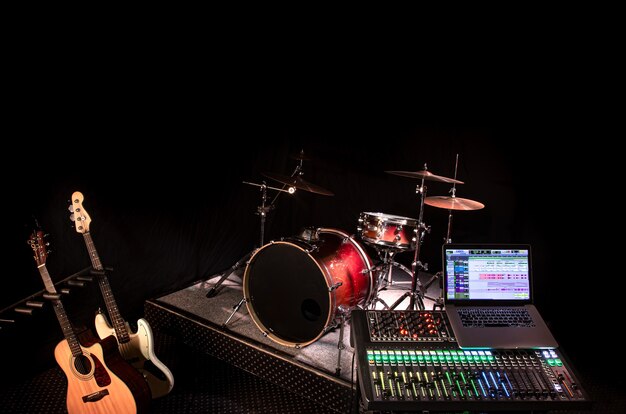 Digitaler Mixer in einem Aufnahmestudio mit einem Computer zum Aufnehmen von Musik. Auf dem Hintergrund eines Schlagzeugs und von Musikinstrumenten. Das Konzept der Kreativität und des Showbusiness.