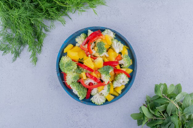 Dill- und Minzbündel neben einer Salatplatte auf Marmorhintergrund. Foto in hoher Qualität