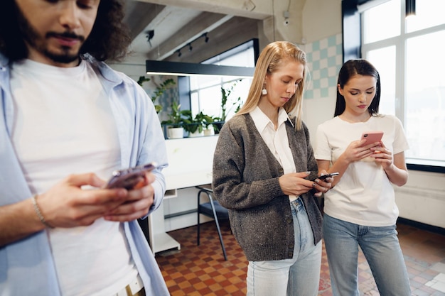 Diverse junge Kollegen, die gemeinsam im Büro an Mobiltelefonen arbeiten