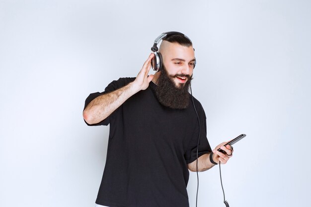 DJ mit Bart, der Kopfhörer trägt und Musik aus seiner Playlist auf seinem Smartphone einstellt.