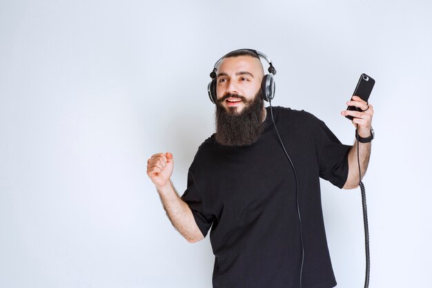 DJ mit Bart trägt Kopfhörer und genießt die Playlist an seinem Handy.