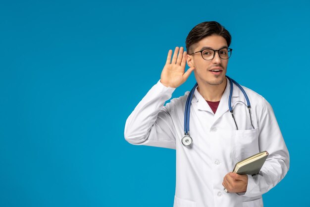 Doctors Day süßer junger gutaussehender Mann in Laborkittel und Brille, der ein Buch belauscht und hält