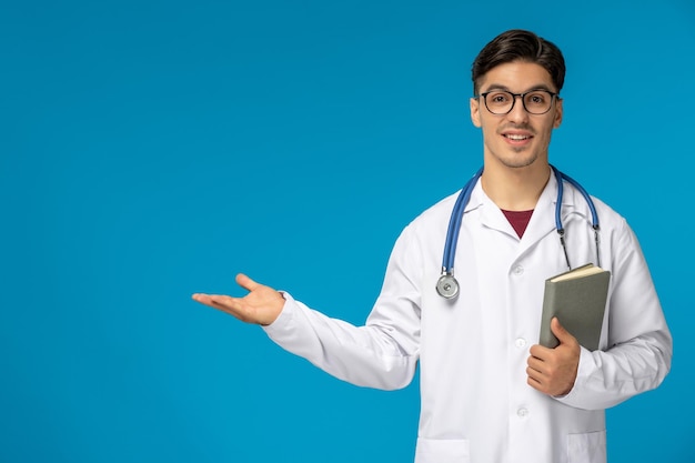 Doctors Day süßer junger gutaussehender Mann in Laborkittel und Brille mit einem Buch