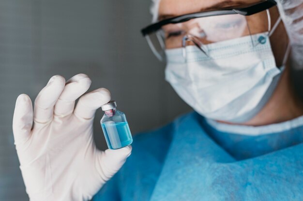 Doktor, der eine Impfflasche hält, während er Schutzausrüstung trägt