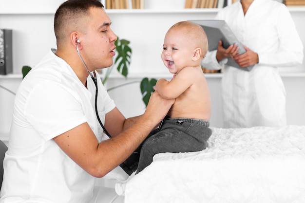 Doktor, der entzückendes kleines Baby mit Stethoskop hört