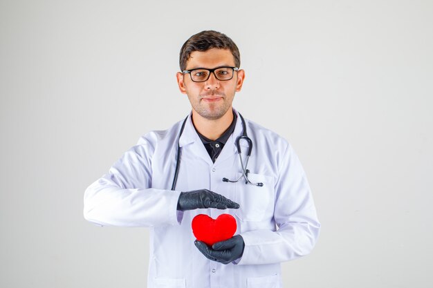 Doktor, der Herz im weißen Kittel mit Stethoskop hält und positiv schaut,