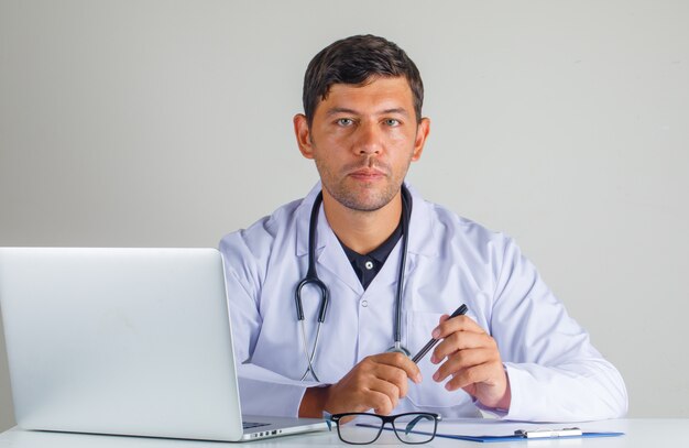 Doktor, der Stift im weißen Kittel und im Stethoskop sitzt und hält