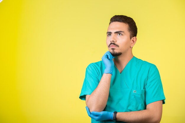 Doktor in Uniform und Handmaske, der nach nirgendwo schaut und überdenkt.