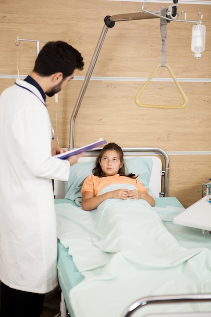 Doktor visint Patientenmädchen im Krankenhaus. Teenager-Mädchen im Krankenhausbett liegend