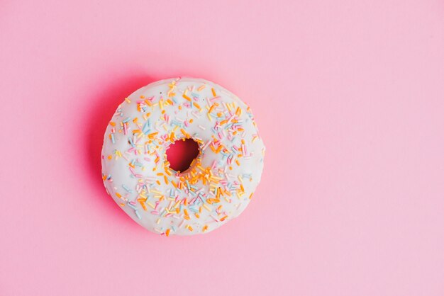 Donut mit bunten Streuseln auf rosa Hintergrund