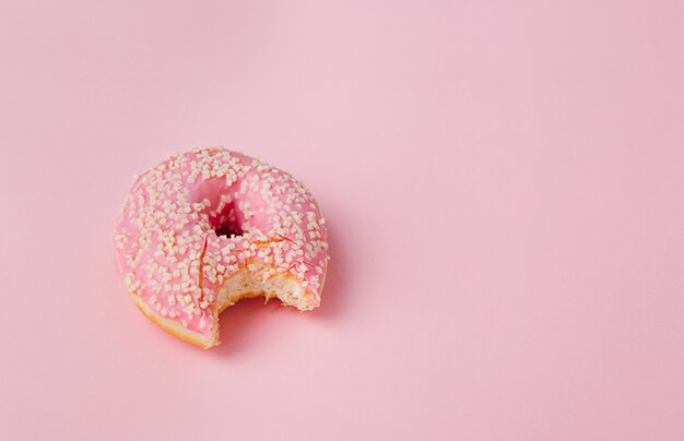 Donuts mit rosa Zuckerglasur auf einem rosa Hintergrund gebissen auf einer Seite