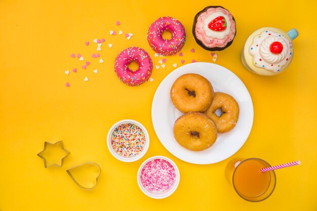 Donuts, Saft, Muffins und Gebäckschneider auf gelbem Hintergrund