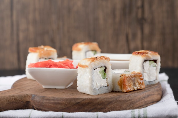 Kostenloses Foto drachen-sushi-rollen mit aal und eingelegtem ingwer auf holzbrett