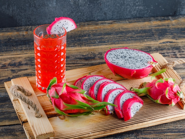 Drachenfrucht mit Saft in einem Tablett auf Holztisch und Gipswand, hohe Winkelansicht.