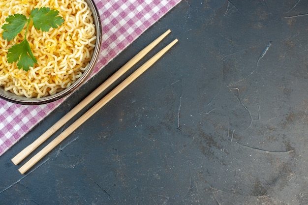 Draufsicht asiatische ramen-nudeln mit koriander in schüssel auf rosa und weiß karierten tischdecken-essstäbchen auf dunklem tisch