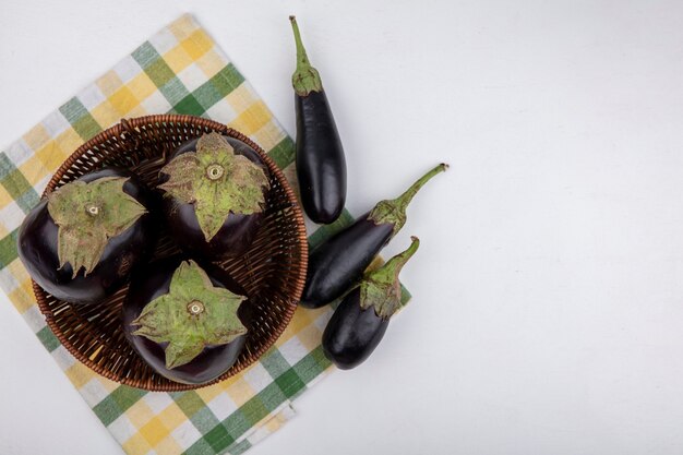 Draufsicht Aubergine in einem Korb auf einem gelben karierten Handtuch auf einem weißen Hintergrund