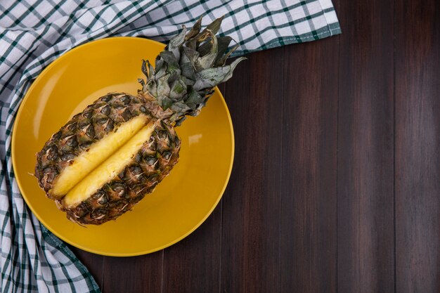 Draufsicht auf Ananas in Platte auf kariertem Stoff und Holzoberfläche