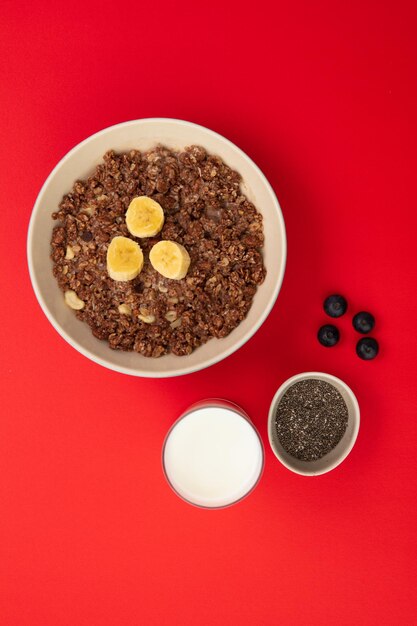 Draufsicht auf Bananen-Walnuss-Haferflocken in Schüssel mit Glas Milchschale mit Chiasamen und Schwarzdornbeeren auf rotem Hintergrund