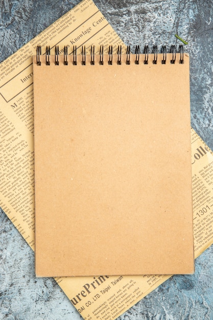 Draufsicht auf braunes Notizbuch auf Zeitung auf grauem Hintergrund