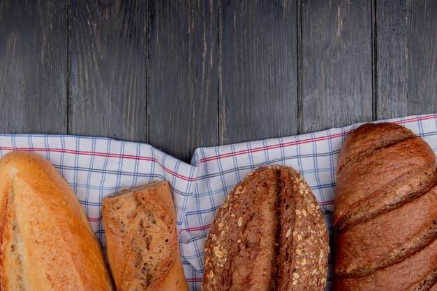 Draufsicht auf Brote als vietnamesische Baguettes mit französischem Samen und Schwarzbrot auf kariertem Stoff und hölzernem Hintergrund mit Kopienraum