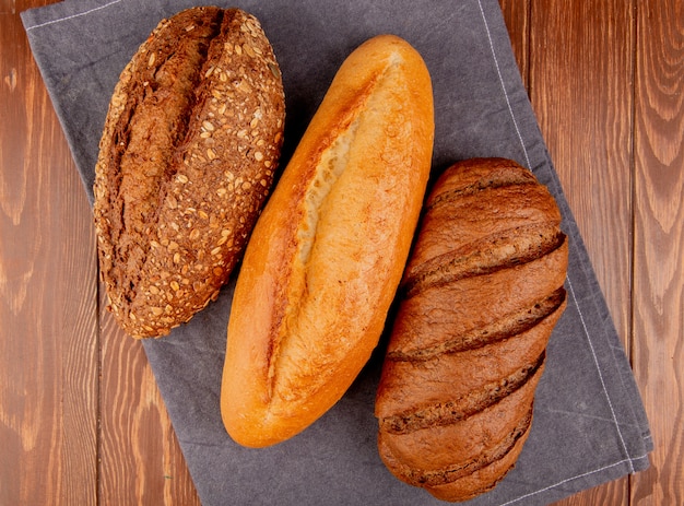 Draufsicht auf Brote als vietnamesisches und schwarzes Baguette und Schwarzbrot auf grauem Stoff und Holztisch