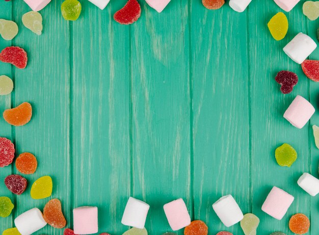 Draufsicht auf bunte leckere Marmeladenbonbons und Marshmallows mit Kopienraum auf Grün
