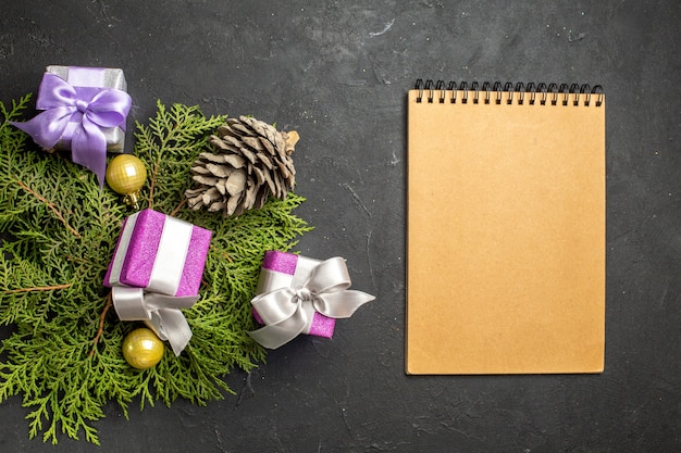 Draufsicht auf bunte Neujahrsgeschenke Dekorationszubehör und Nadelbaumkegel neben Notebook auf dunklem Hintergrund