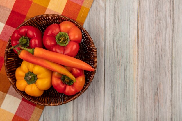 Draufsicht auf bunte Paprika mit süßem Geschmack auf einem Eimer auf einem karierten Tuch auf einer grauen Holzoberfläche mit Kopierraum