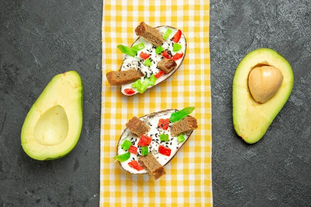 Draufsicht auf cremige Avocados mit Brot und Pfeffer auf grauer Oberfläche